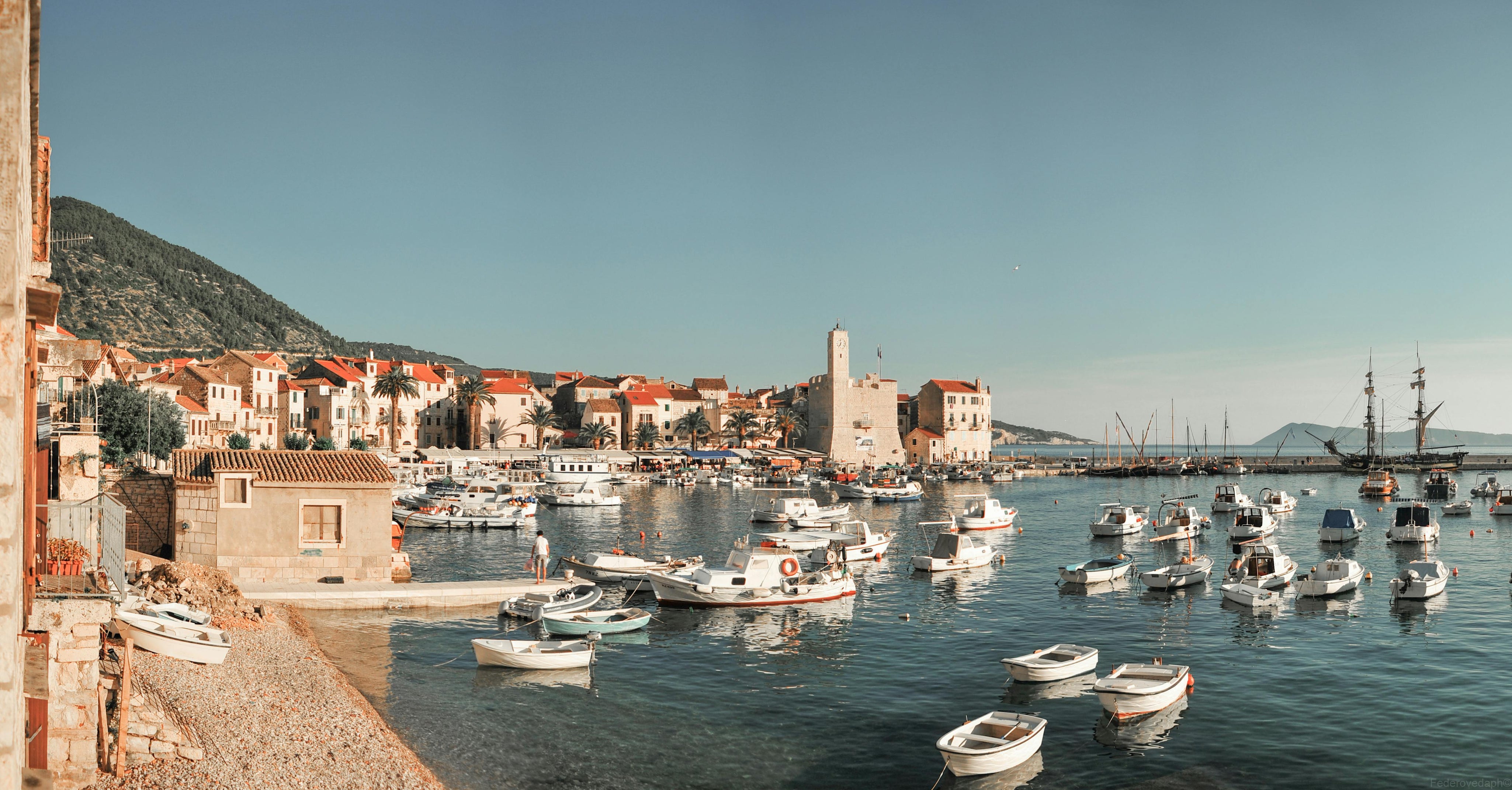 FRENKY travel bag resting on a stone wall overlooking the Dalmatian coastline and crystal-clear water.