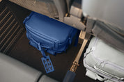 A blue soft-sided bag with a hanging tag reading ENKY, placed under a seat in a real-world travel setting next to another bag.